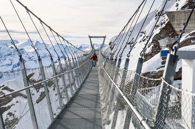 Looking along a steel-mesh suspension bridge towards snowfields and peaks