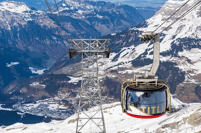 A round cable car cabin passing a pylon, with a green valley far below