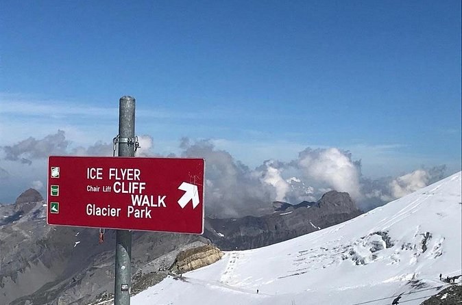 A red signpost pointing to the chairlift, the bridge and the snow park above a glacier