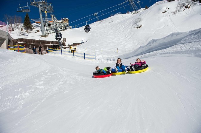 Riders on inflatable snow tubes sliding down a groomed slope below a chairlift