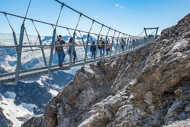 Walkers crossing a narrow suspension bridge strung across a snowy rock face
