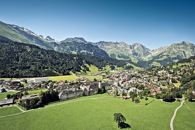A valley village spread across green meadows below forested slopes and rock peaks